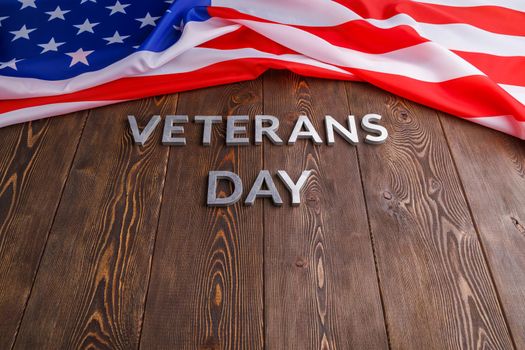 the words veterans day laid with silver metal letters on wooden board surface with crumpled usa flag.