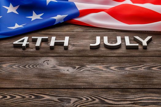 the words 4th july and crumpled usa flag on flat textured wooden surface background.