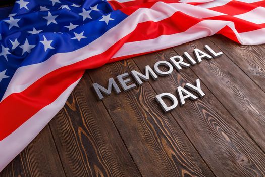 the words memorial day laid with silver metal letters on wooden board surface with crumpled usa flag below with diagonal perspective