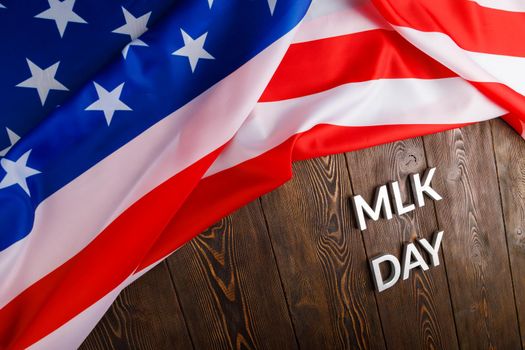 the word MLK day laid with silver metal letters on wooden surface with crumpled USA flag at upper side in diagonal perspective. MLK means Martin Luther King Jr.