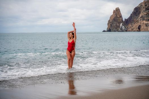 A beautiful and sexy brunette in a red swimsuit on a pebble beach, Running along the shore in the foam of the waves.