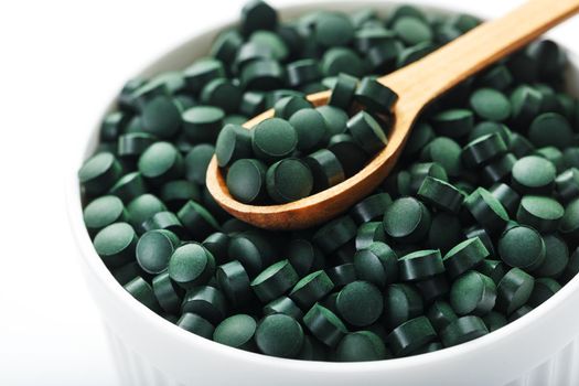 Organic spirulina tablets in a white cup with a wooden spoon on a white background with free space top view