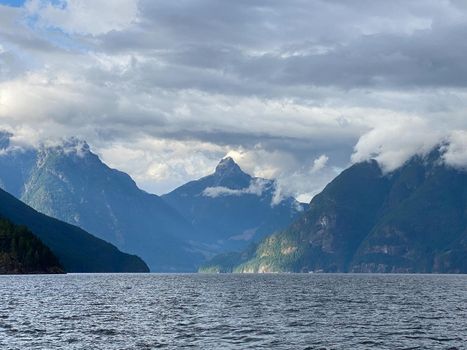 Jervis Inlet north in British Columbia, surrounded by high, rugged peaks of the Coast Mountains and beautiful water clouds in the sky. Inlet approach to Malibu Rapids