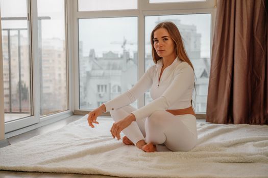 Side view portrait of relaxed woman listening to music with headphones lying on carpet at home. She is dressed in a white tracksuit