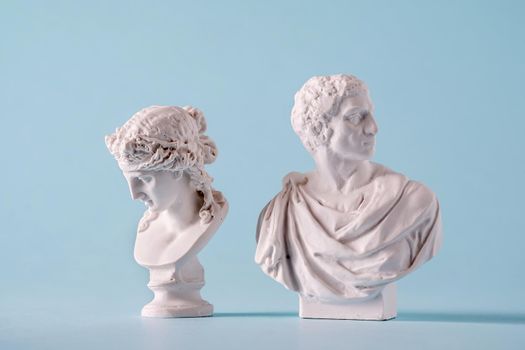 Two white Roman or Grecian antique style busts of young men over a blue background