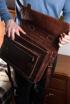 Details of open empty brown men's shoulder leather bag for a documents and laptop on the shoulders of a man in a blue shirt . mens leather handmade briefcase.