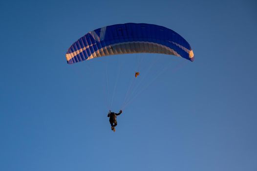 Silhouette of a man on a paraglider flying in the blue sky