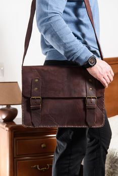 Side view of man in a blue sweater with brown leather briefcase. Retro style. Unisex bag for sale. Indoor photo