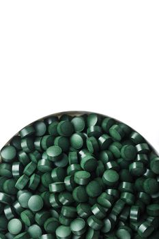 Green tablets made of natural organic spirulina in a cup on a white background with free space top view