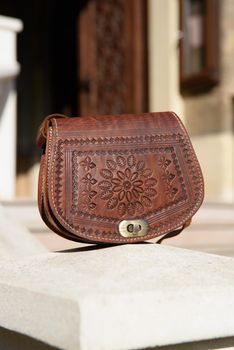 small brown women's leather bag with a carved pattern. street photo