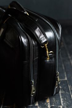 Leather black travel bag, on a black wooden floor. soft light