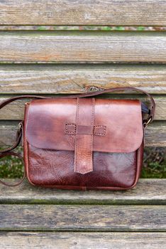 close-up photo of brown leather handbag on a wooden bench. Outdoors photo