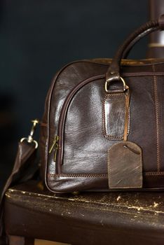 Leather brown travel bag, on a brown leather chair. Indoor photo. soft light