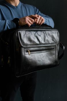 Man holding black leather travel bag. Soft light. Indoor photo