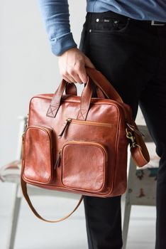 Side view of man in a blue sweater with red leather briefcase. Retro style. Unisex bag for sale. Indoor photo