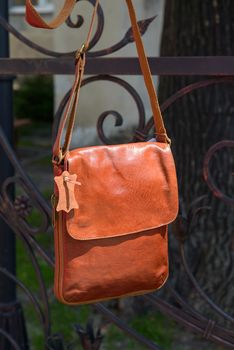 Outdoor photo of a orange leather Messenger bag. Close up.