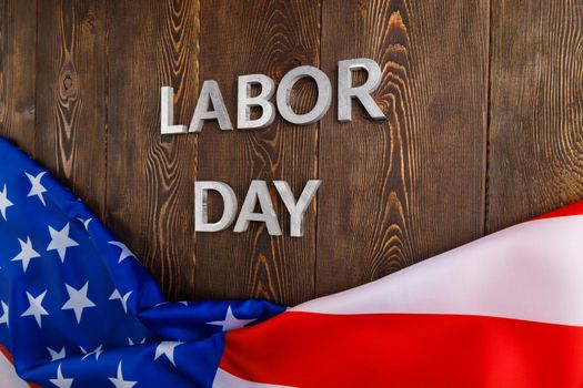 words labor day laid with silver metal letters on wooden surface with crumpled USA flag on bottom side in diagonal perspective