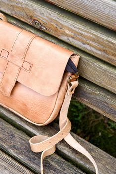 close-up photo of yellow leather handbag on a wooden bench. Outdoors photo
