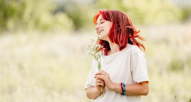 Teen girl with red hair at the nature smiling with bouquet in hands. Pretty young female in the sunny field