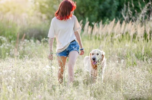 Teen girl walking with golden retriever dog at the nature. Pretty young female with doggy pet in the field at summer
