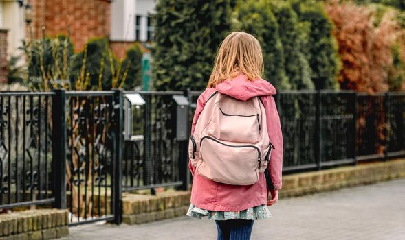 School girl with backpack walks at street. Preteen child kid outdoors after college class, view from back