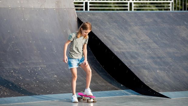 Preteen girl riding on skateboard at park ramp. Beautiful female child skater with board outdoors