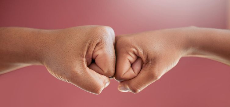 Cropped shot of two unrecognizable people fist bumping in studio against a red background.