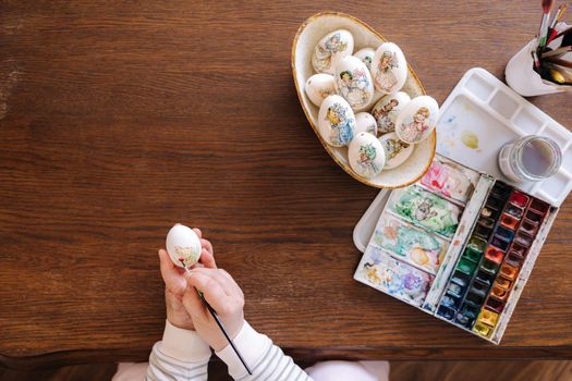 Top view of woman painting a water colors on fantasy chicken eggs for Easter egg festival. Female drawing little yellow chick. The symbolic of spring. Easter concept.