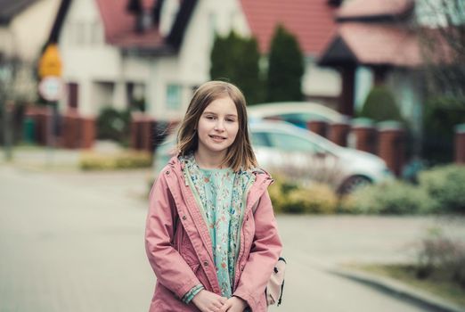 School girl with backpack walks at street. Preteen child kid posing outdoors after college class