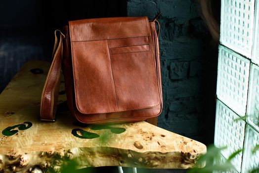 close-up photo of orange leather messanger bag on a wooden table. indoor photo