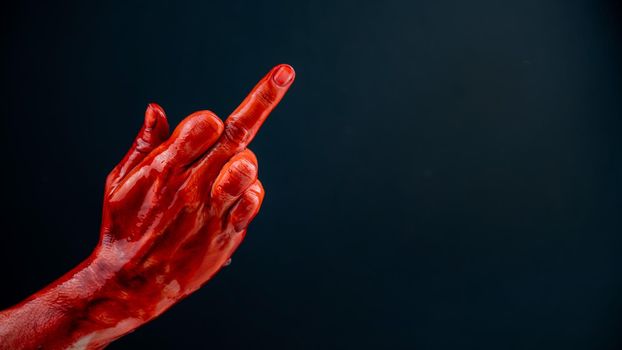 Female hand stained with blood shows the middle finger on a black background