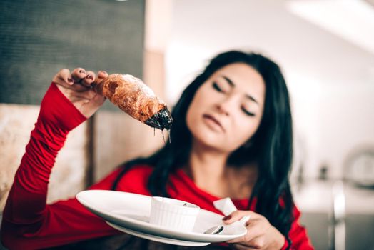 sexy woman in a red dress with black hair eats a croissant. temptation with food. attractive legs. obsession with red. Selective focus