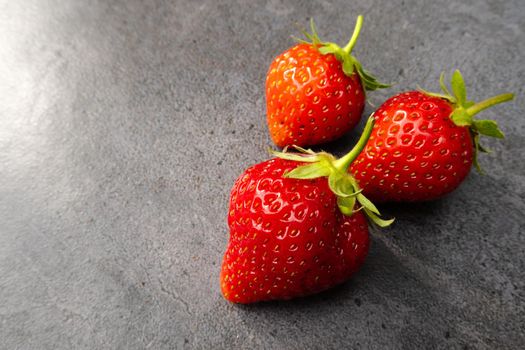 Three  red ripe strawberries over dark background with copy space