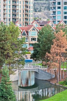 Facades of residential apartment buildings with water channel and green lawn in front. Low-rise condo building on high-rise tower backgfound