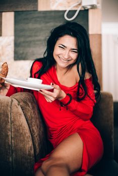 sexy woman in a red dress with black hair eats a croissant. temptation with food. attractive legs. obsession with red. Selective focus