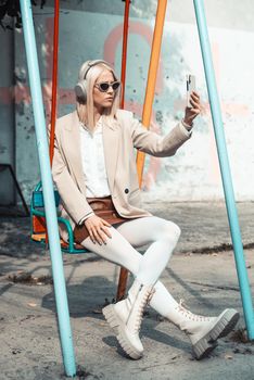 Young smiling cheerful woman outdoors using social media apps on phone for video chatting and stying connected. woman wearing white jacket, blouse, tights and brown leather skirt