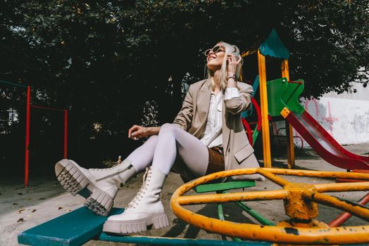 Portrait of blonde hipster fashion model wear stylish wireless headphones enjoy listen new cool music. woman wearing white jacket, blouse, tights and brown leather skirt