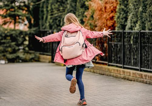 School girl with backpack running at street. Preteen child kid happy outdoors after college class, view from back