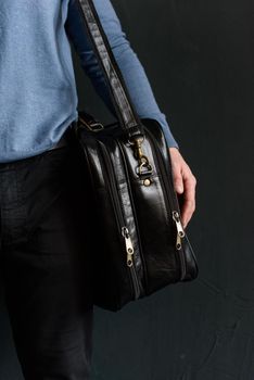 Man holding black leather travel bag. Soft light. Indoor photo