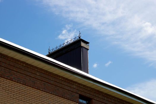 A roof with a chimney on the background of a blue summer sky