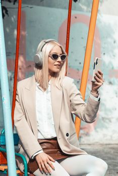 Young smiling cheerful woman outdoors using social media apps on phone for video chatting and stying connected. woman wearing white jacket, blouse, tights and brown leather skirt