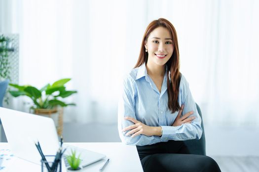 An Asian entrepreneur or businesswoman shows a smiling face while working with using computer on a wooden table