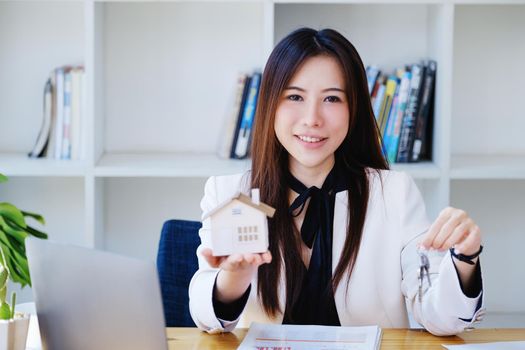 Accountant, businessman, real estate agent, Asian business woman handing house keys to customers along with house interest calculation documents for customers to sign