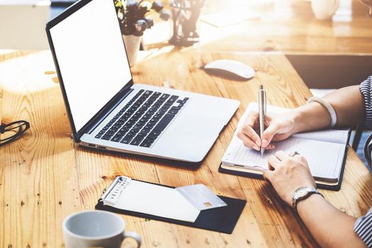 learning, note taking, planning, female employee holding a pen to write a notebook and using a computer to learn how to plan, invest and manage financial risks