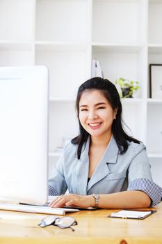 An Asian entrepreneur or businesswoman shows a smiling face while working with using computer on a wooden table