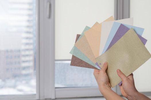 Woman holding fabric samples of roller blinds against window background