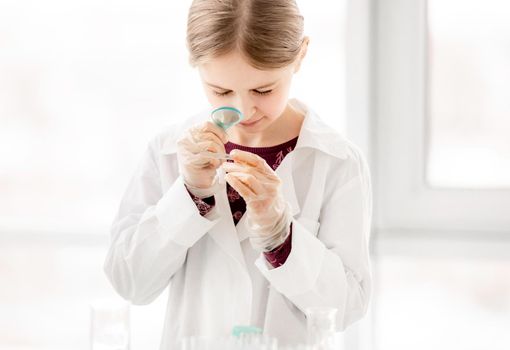 Smart girl during scientific chemistry experiment looking at glass with tests. Schoolgirl with chemical equipment on school lesson