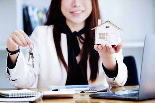 Accountant, businessman, real estate agent, Asian business woman handing house keys to customers along with house interest calculation documents for customers to sign