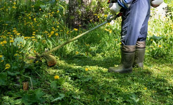 Man mows grass with a gasoline scythe.