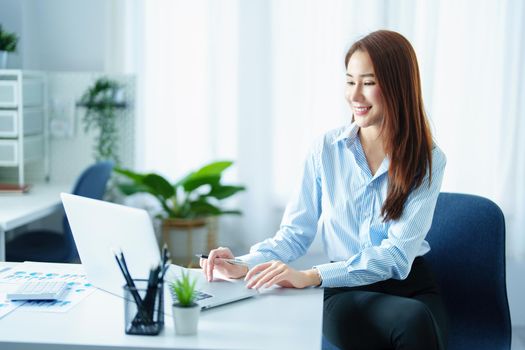 An Asian entrepreneur or businesswoman shows a smiling face while working with using computer on a wooden table